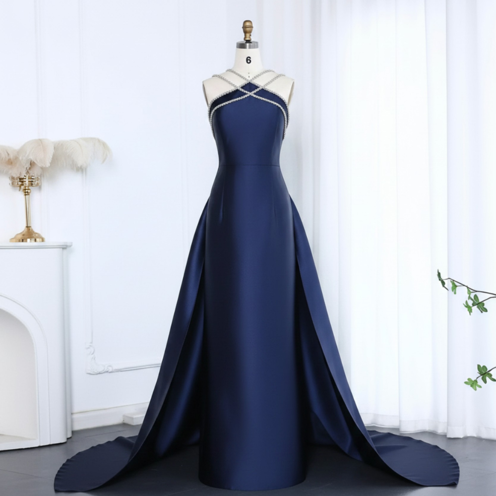 Navy blue satin mermaid evening gown with a beaded halter neckline, open overskirt, and floor-length train on a mannequin.