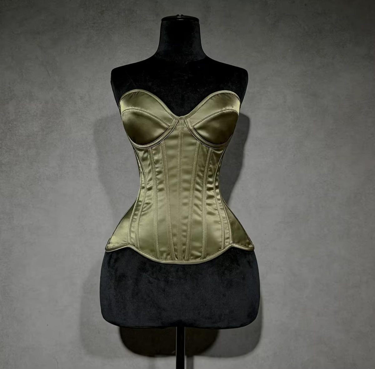 Olive green satin overbust corset with structured cups and steel boning on a black mannequin display.