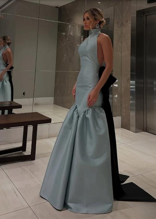 Baby blue satin mermaid evening gown with a high collar, open back, and a dramatic black bow detail.