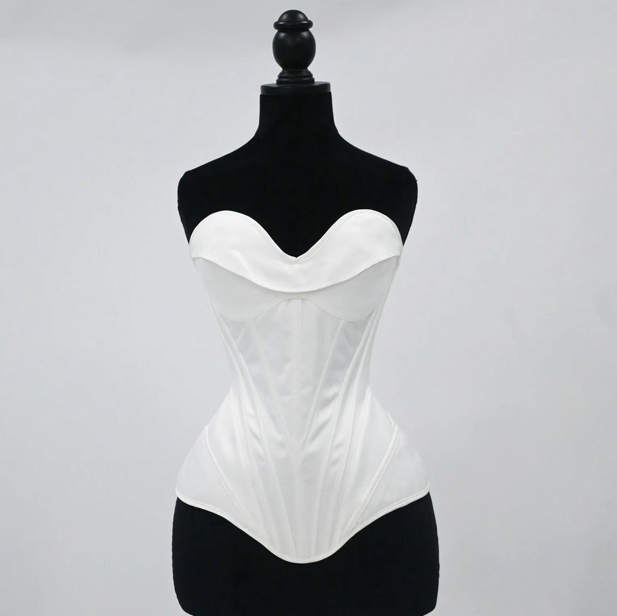 White satin bridal corset bustier with structured boning and a sweetheart neckline on a black mannequin.