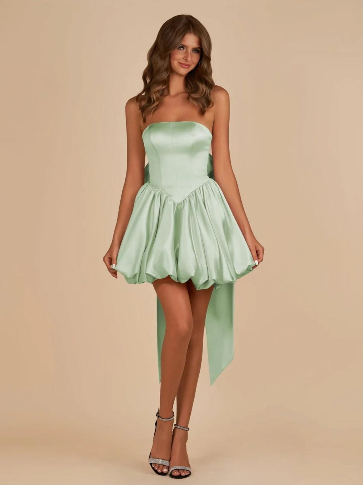 Sage green satin mini dress with a strapless corset bodice, voluminous skirt, and a large detachable back bow.