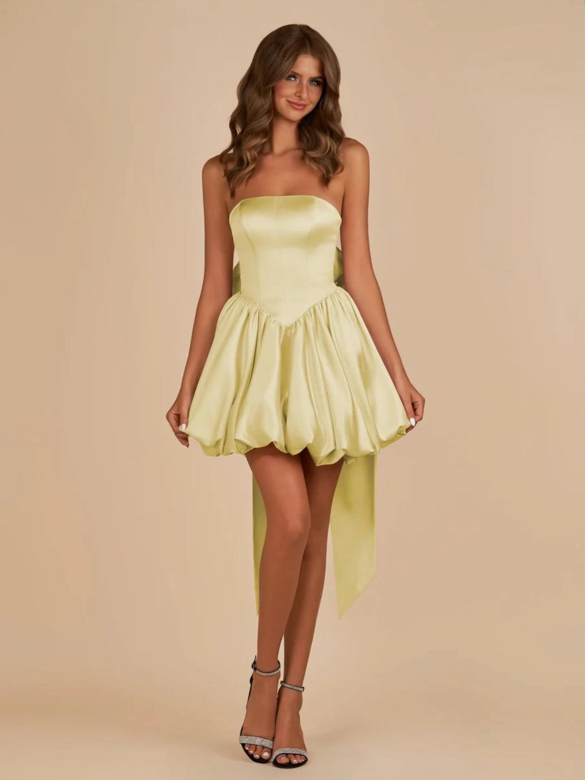 Pale yellow satin mini dress with a strapless corset bodice, voluminous skirt, and a large detachable back bow.