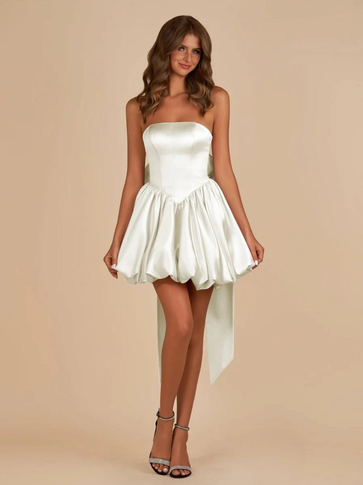 White satin mini dress with a strapless corset bodice, voluminous bubble skirt, and a large detachable back bow.