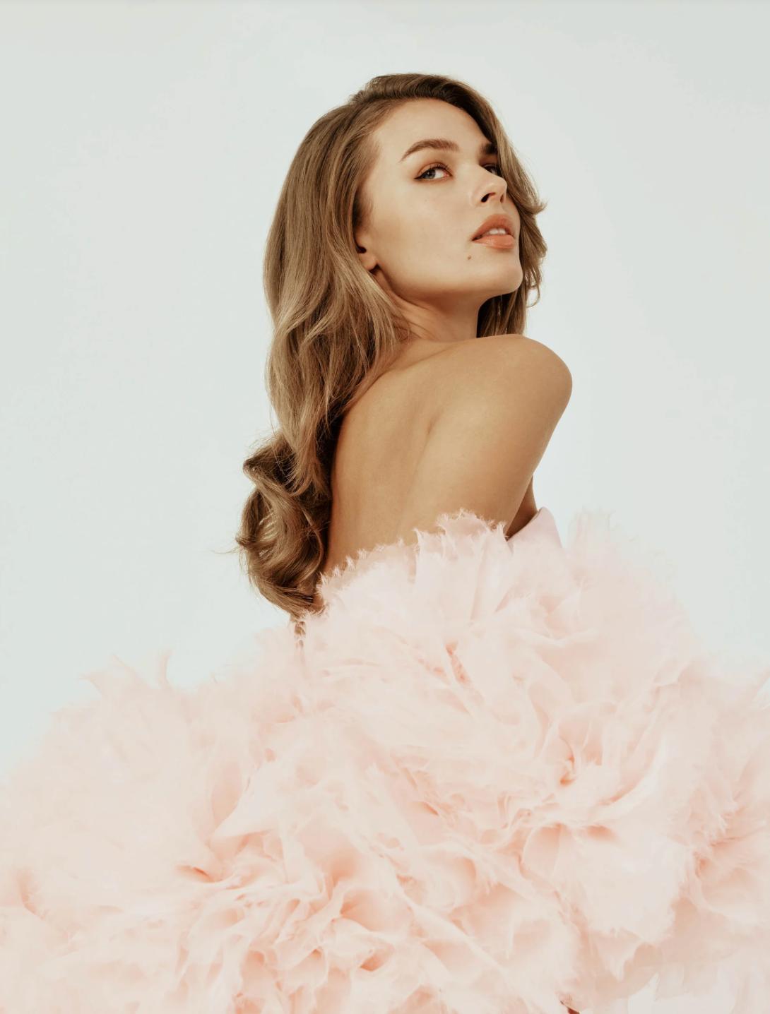 Model wearing a strapless Berlin gown featuring a sculptural, pale pink organza cape with hand-crafted floral details.