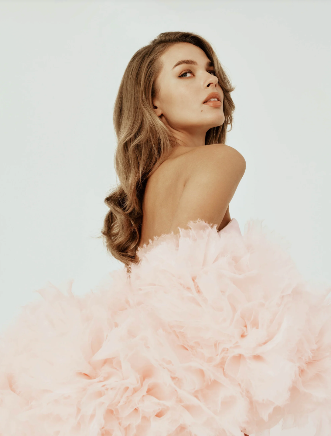 Model wearing a strapless Berlin gown featuring a sculptural, pale pink organza cape with hand-crafted floral details.
