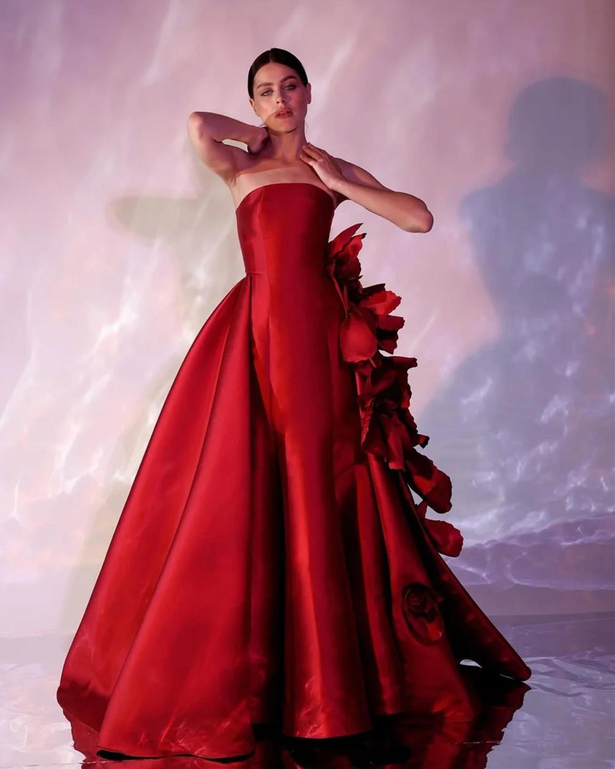 Strapless red satin column gown with a voluminous overskirt and dramatic 3D floral accents for formal events.