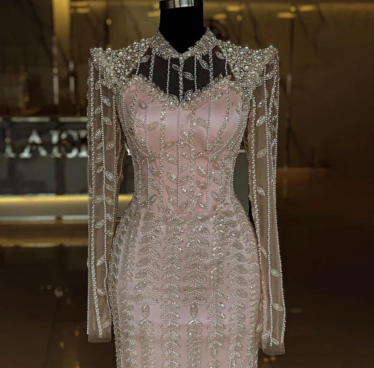 Blush pink mermaid gown featuring intricate crystal and pearl beading, long sheer sleeves, and a high o-neck design.
