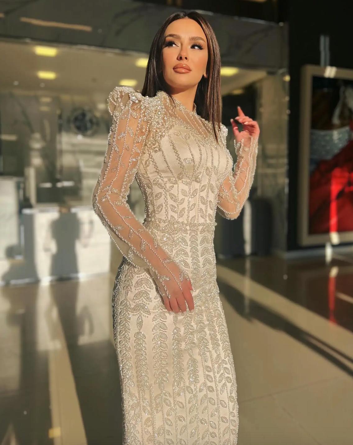 Beige mermaid gown with intricate pearl and crystal beading, long sheer sleeves, and a structured o-neck design.