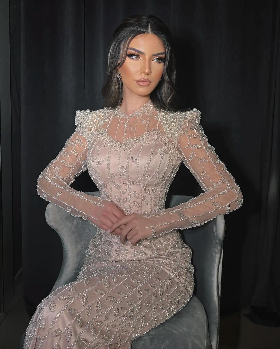 Beige mermaid gown featuring intricate pearl and crystal beading, long sleeves, and a high o-neck on soft tulle fabric.
