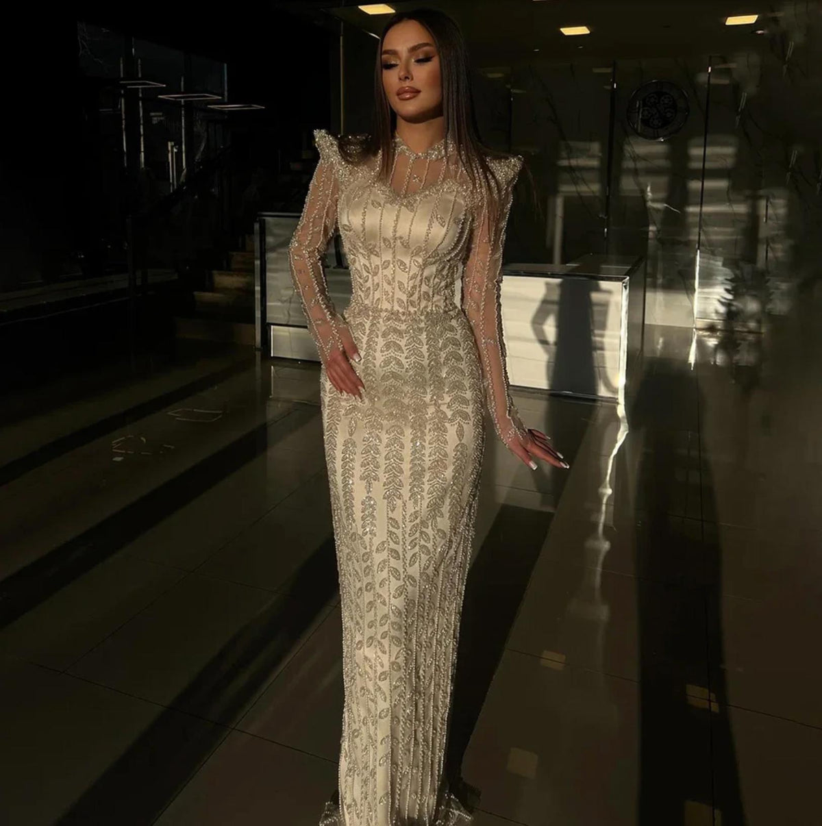 Ivory mermaid gown with intricate pearl and crystal beading, long sheer sleeves, and a high o-neck design.