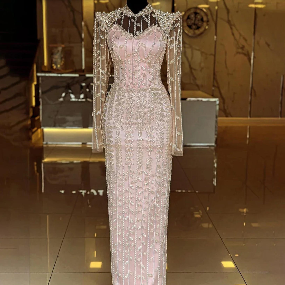 Blush pink mermaid gown featuring intricate pearl and crystal beading, sheer long sleeves, and a high o-neck design.