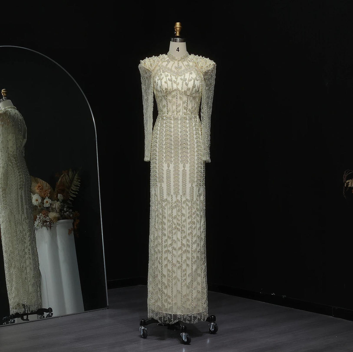 Cream mermaid gown with long sleeves, intricate pearl and crystal beading, and a high neck on a mannequin.