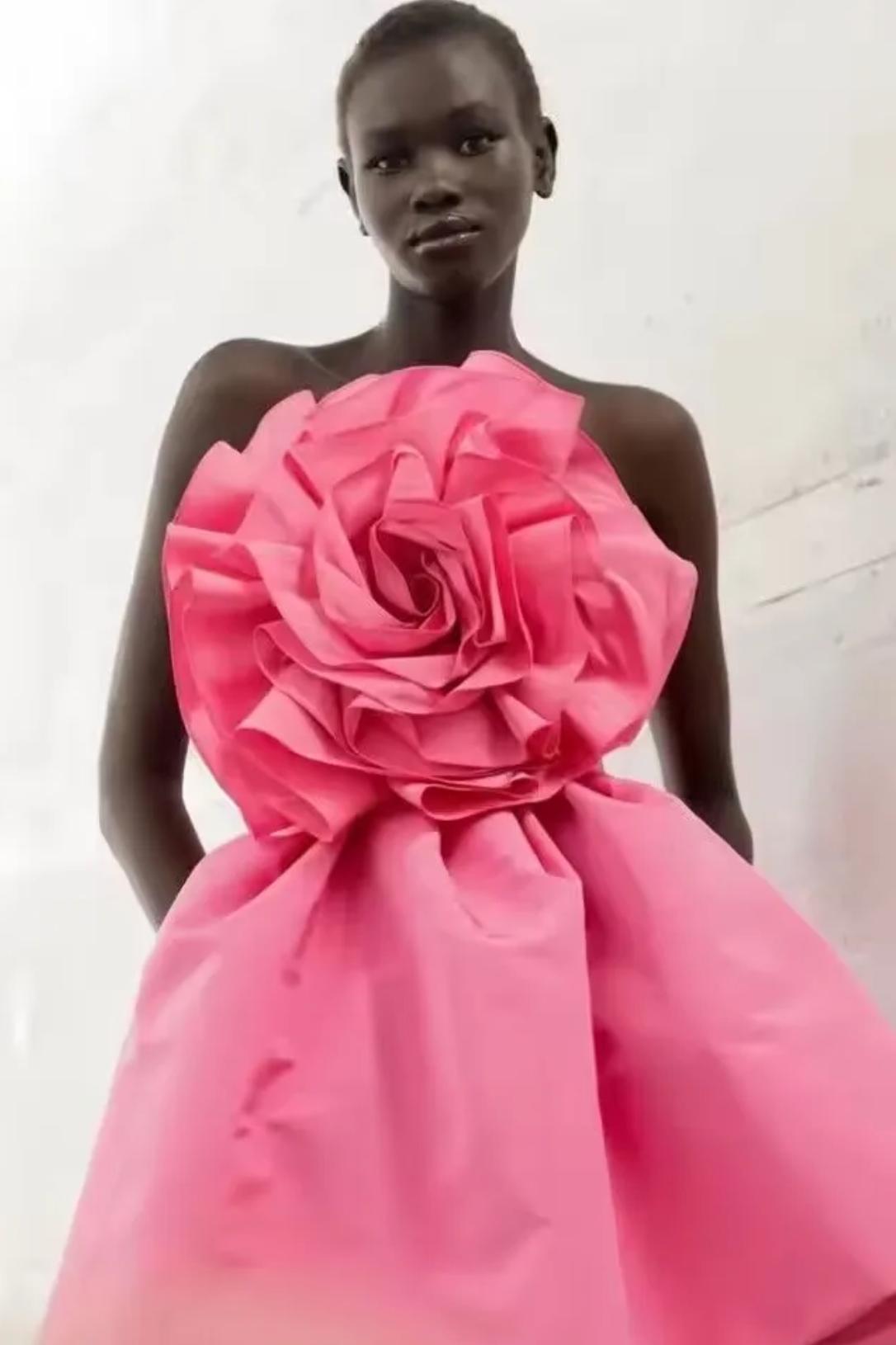 Model wearing a sleeveless pink satin mini party dress featuring a large 3D rose decoration on the bodice.