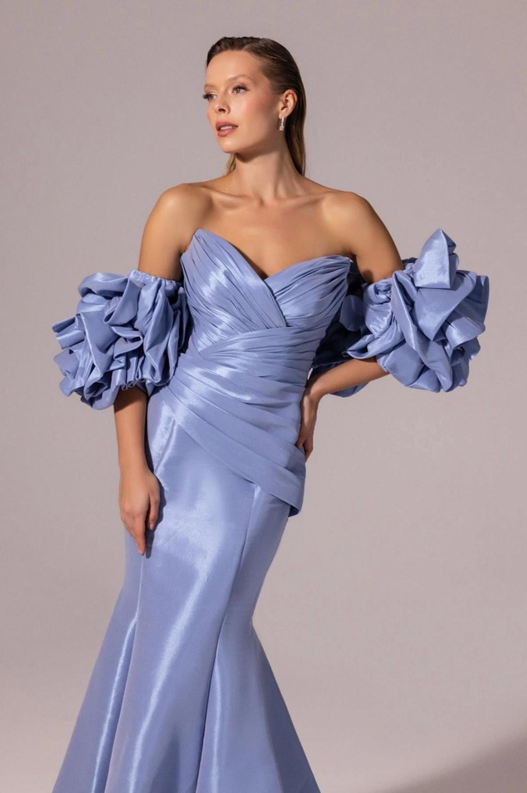 Periwinkle satin mermaid gown with off-the-shoulder ruffled sleeves, a draped V-neck bodice, and a floor-length silhouette.