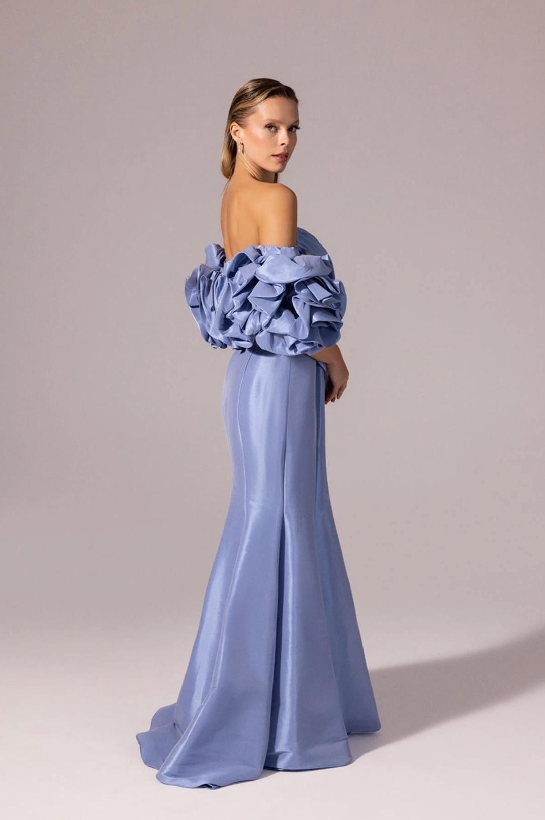 Periwinkle blue floor-length mermaid gown in satin with off-the-shoulder ruffled sleeves and a sleek silhouette.