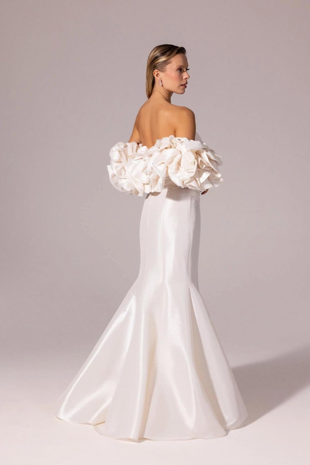 White satin mermaid gown with off-the-shoulder ruffled sleeves and a floor-length silhouette.