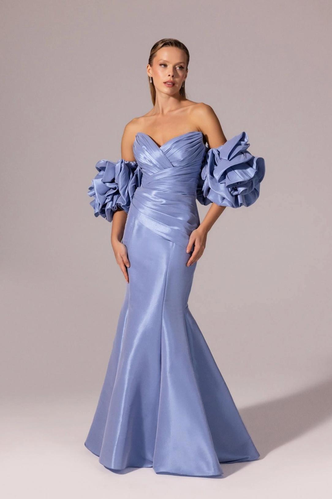 Periwinkle blue floor-length mermaid gown in satin with off-the-shoulder ruffled sleeves and a structured V-neck bodice.
