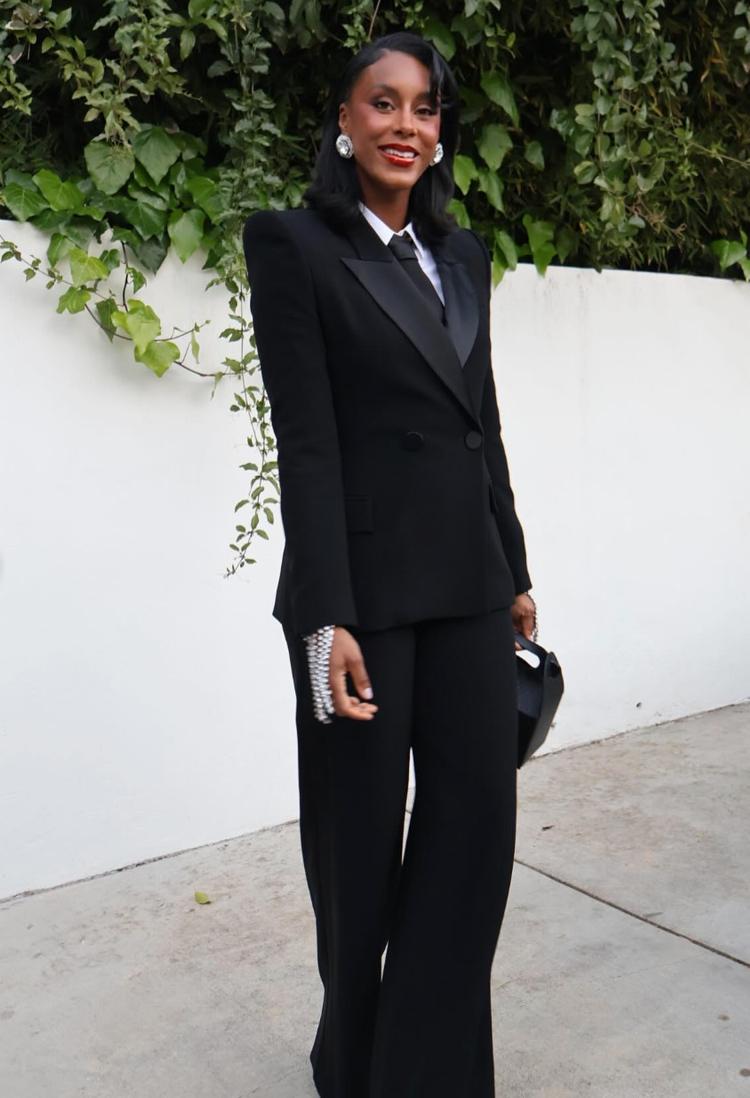 Woman wearing a black Brioni Vanqui double-breasted suit with satin peaked lapels, white shirt, and tailored trousers.