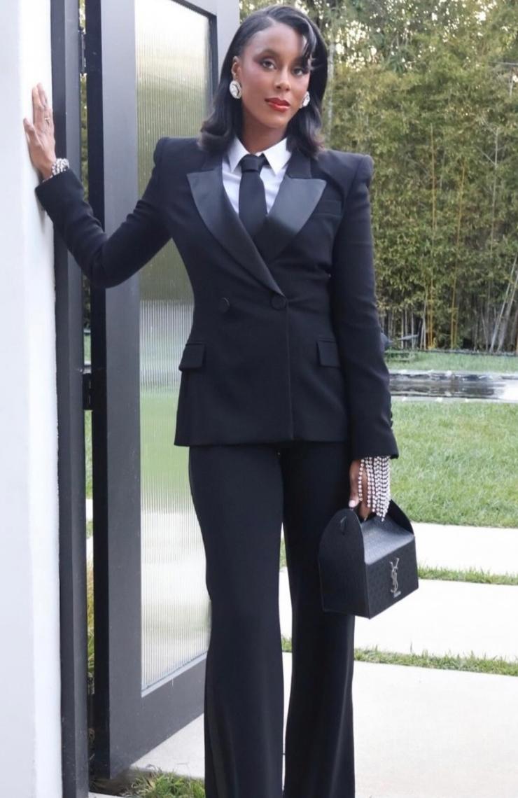 Woman wearing a black double-breasted Brioni Vanqui suit with satin peaked lapels, white shirt, and black tie.