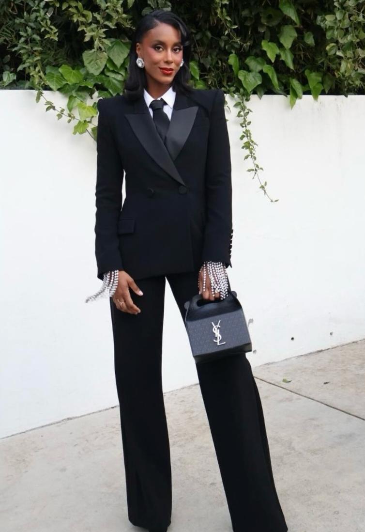 Woman wearing a black double-breasted Brioni Vanqui suit with satin peaked lapels, white shirt, tie, and crystal sleeve cuffs.