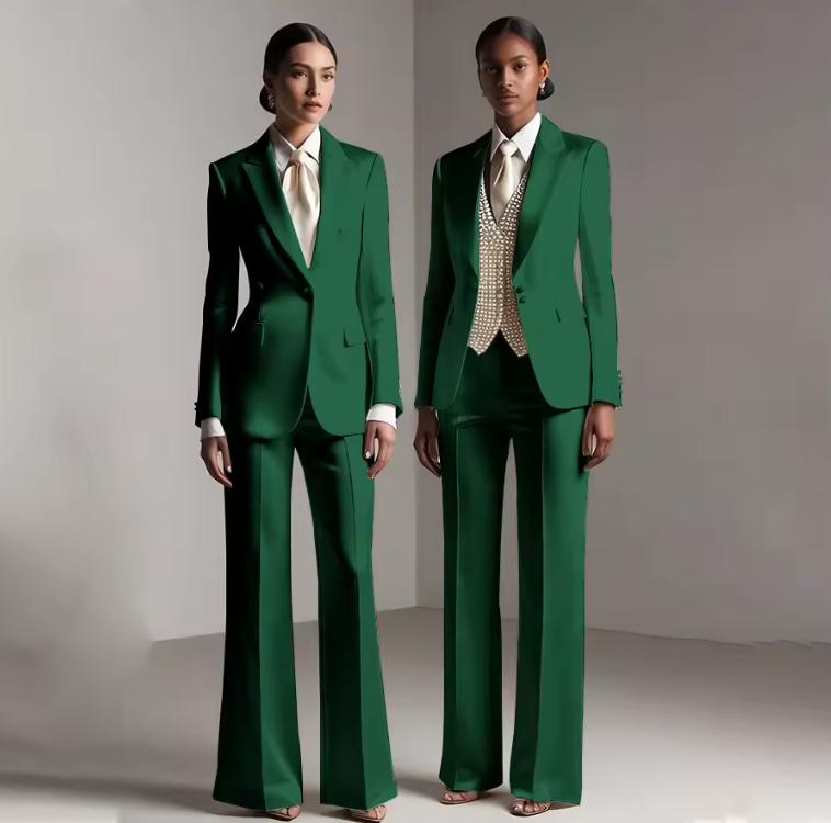 Two models wearing tailored emerald green satin pantsuits with single-breasted jackets and wide-leg trousers.