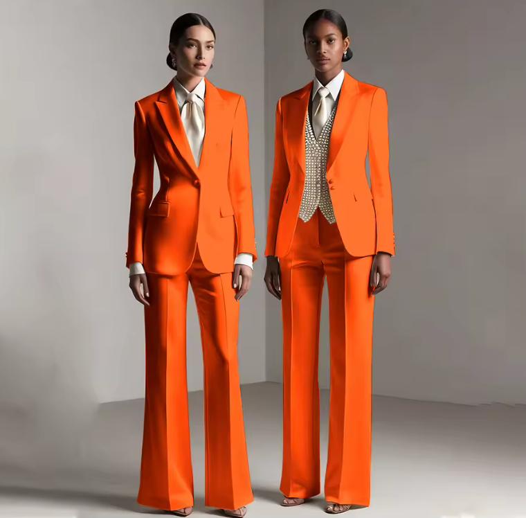 Two models wearing vibrant orange satin single-breasted pantsuits with tailored jackets and wide-leg trousers.