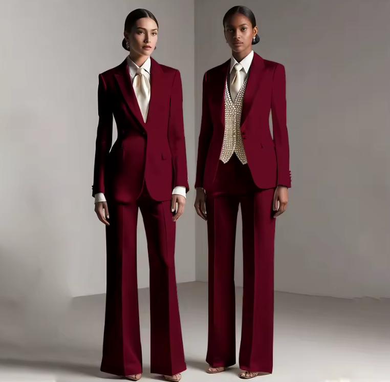 Two models wearing tailored burgundy satin pantsuits with single-breasted jackets and coordinating trousers.