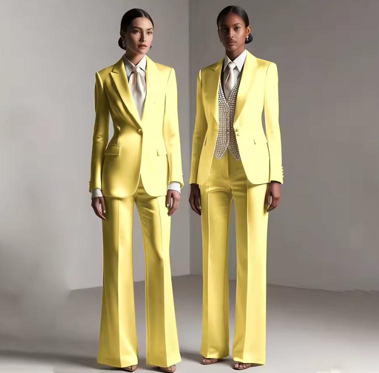 Two models wearing tailored yellow satin single-breasted pantsuits with wide-leg trousers and white collared shirts.
