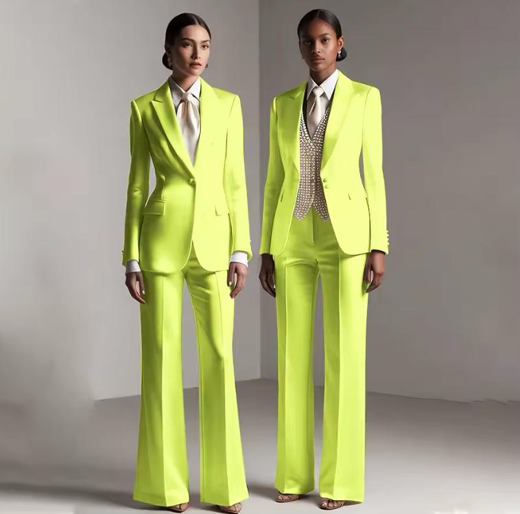 Two models wearing vibrant neon yellow satin single-breasted pantsuits with tailored jackets and matching trousers.