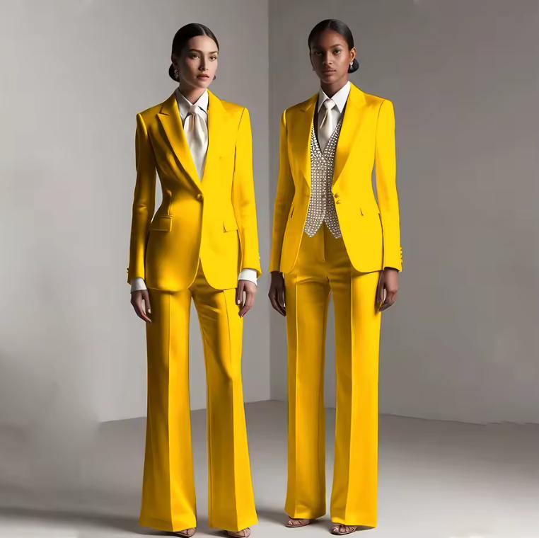 Two models wearing vibrant yellow satin single-breasted pantsuits with tailored jackets and matching trousers.