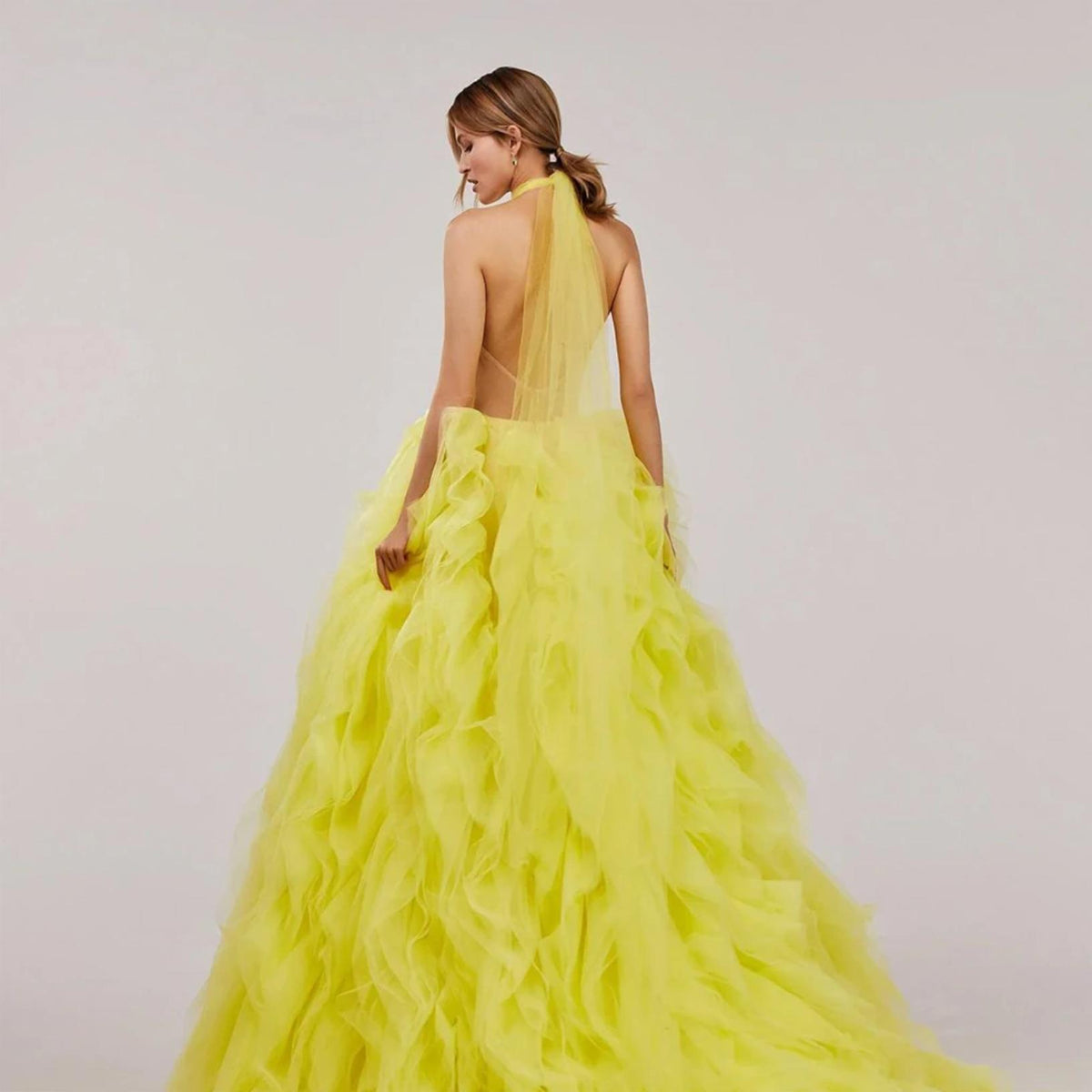 Back view of a vibrant yellow halter ball gown featuring tiered tulle pleating and a dramatic floor-sweeping train.