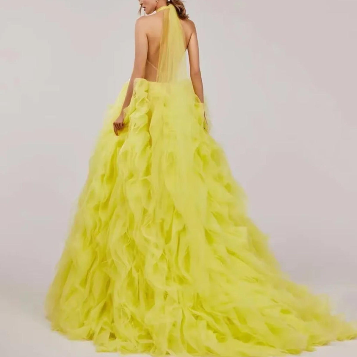 Back view of a chartreuse yellow halter ball gown with tiered tulle ruffles and a dramatic floor-sweeping train.
