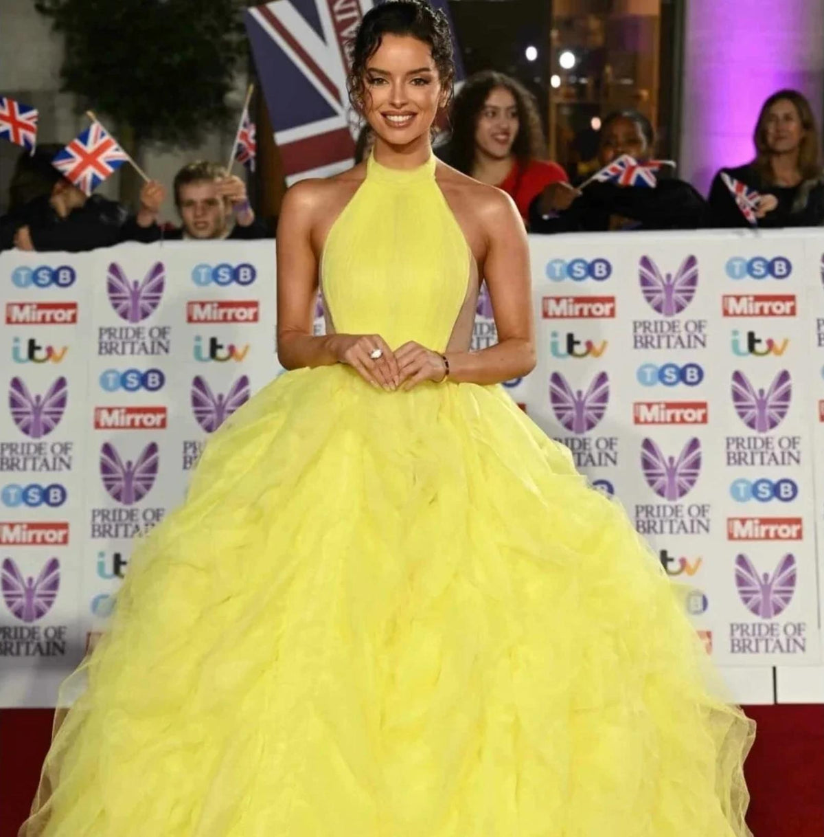 Bright yellow halter ball gown with tiered tulle pleating and a dramatic floor-sweeping silhouette on a red carpet.