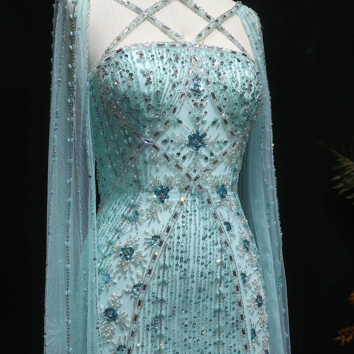 Light blue tulle mermaid gown with a criss-cross neckline, cape sleeves, and intricate crystal and sequin beadwork.