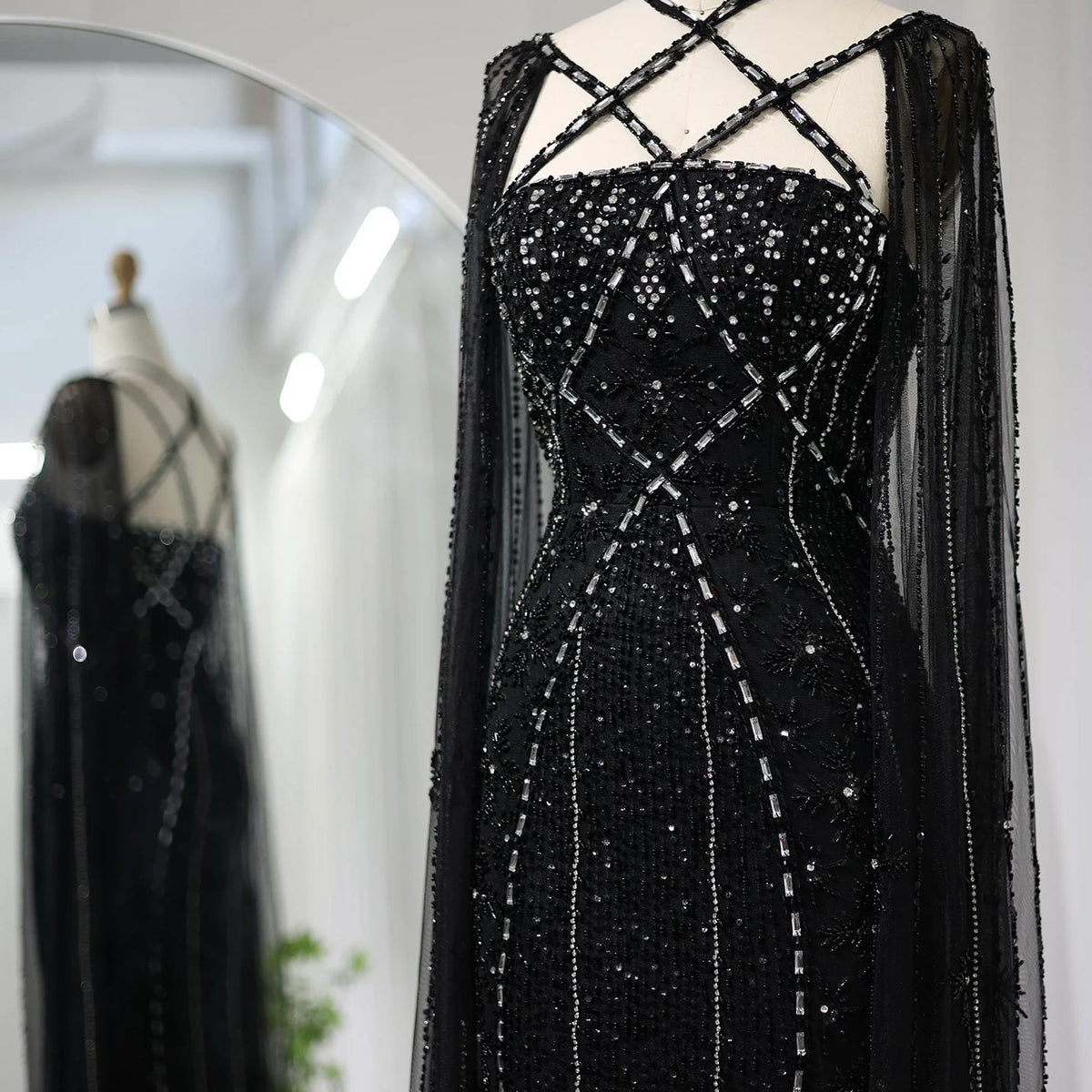 Black mermaid gown with a criss-cross neckline, cape sleeves, and intricate crystal and sequin beadwork on tulle.
