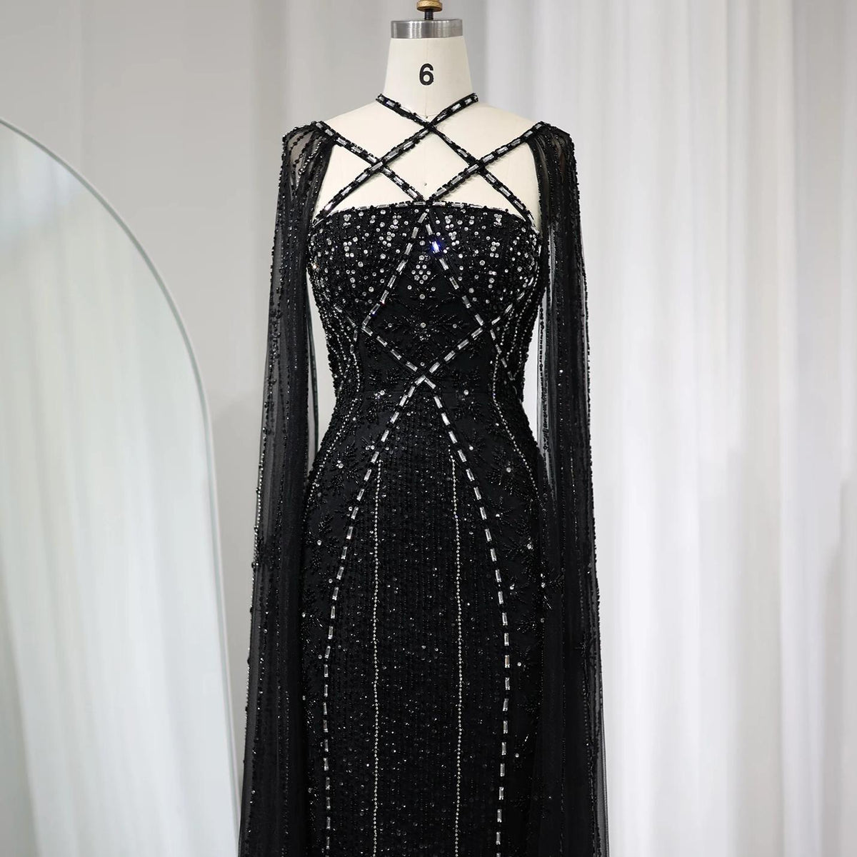 Black mermaid gown with cape sleeves, criss-cross neckline, and intricate crystal and sequin beadwork on tulle.