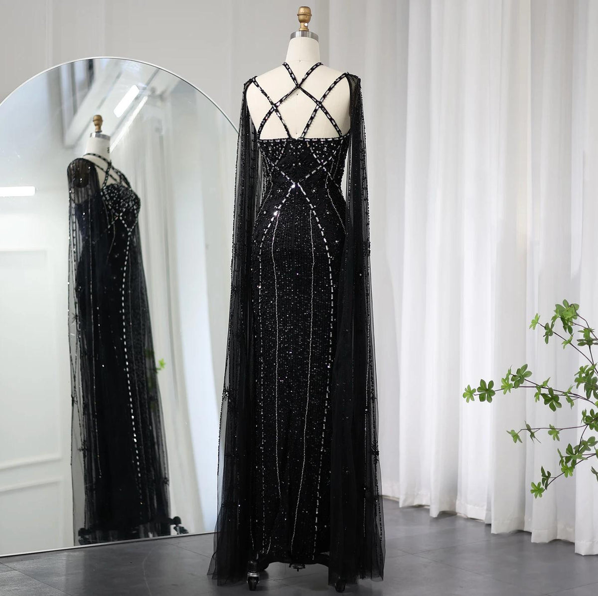 Black mermaid gown with cape sleeves, criss-cross back, and intricate crystal and sequin embellishments on tulle.