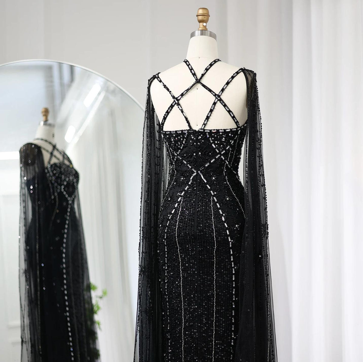 Black mermaid gown with cape sleeves, criss-cross back, and intricate crystal and sequin embellishments on tulle.