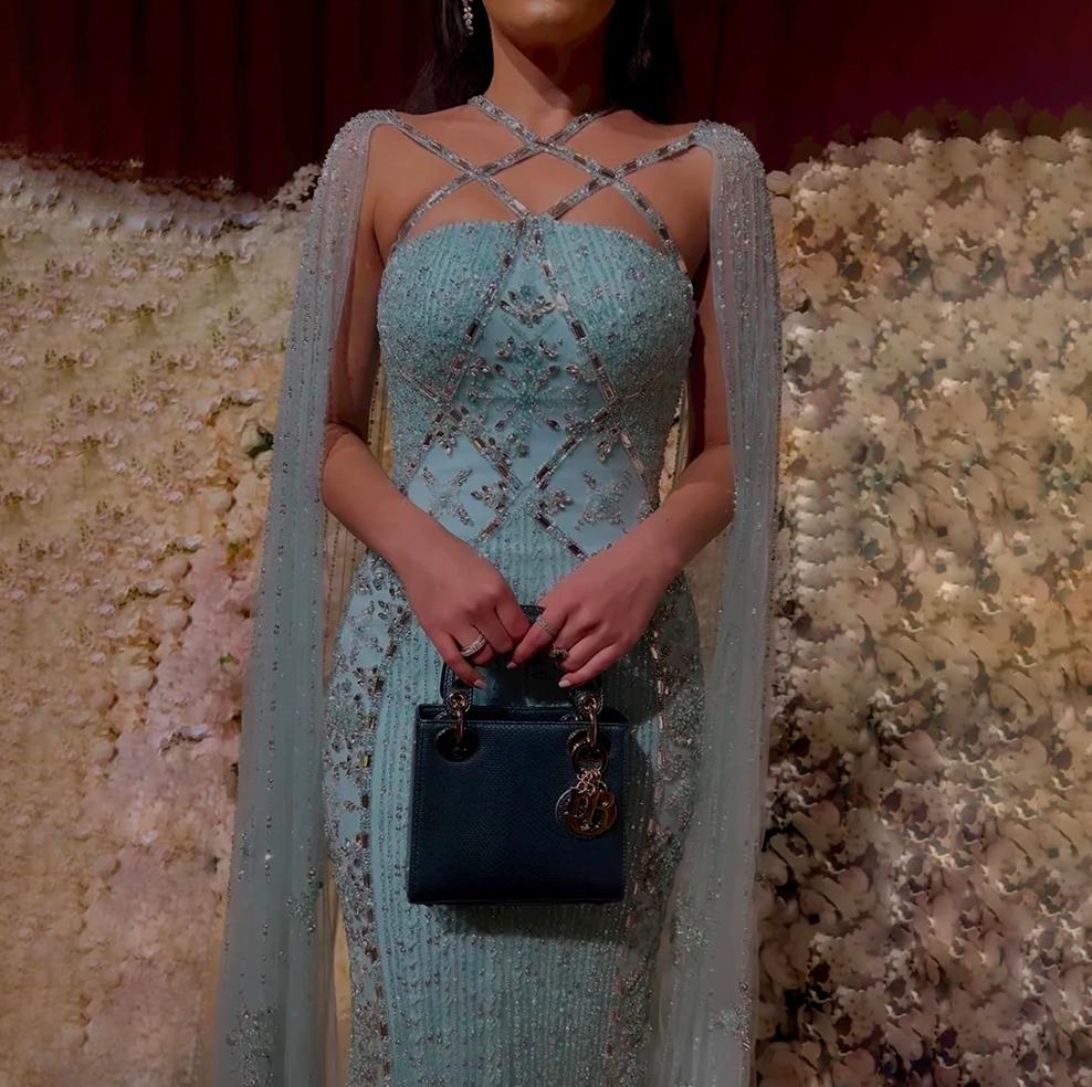 Light blue mermaid gown with a criss-cross neckline, cape sleeves, and intricate crystal and sequin embellishments.