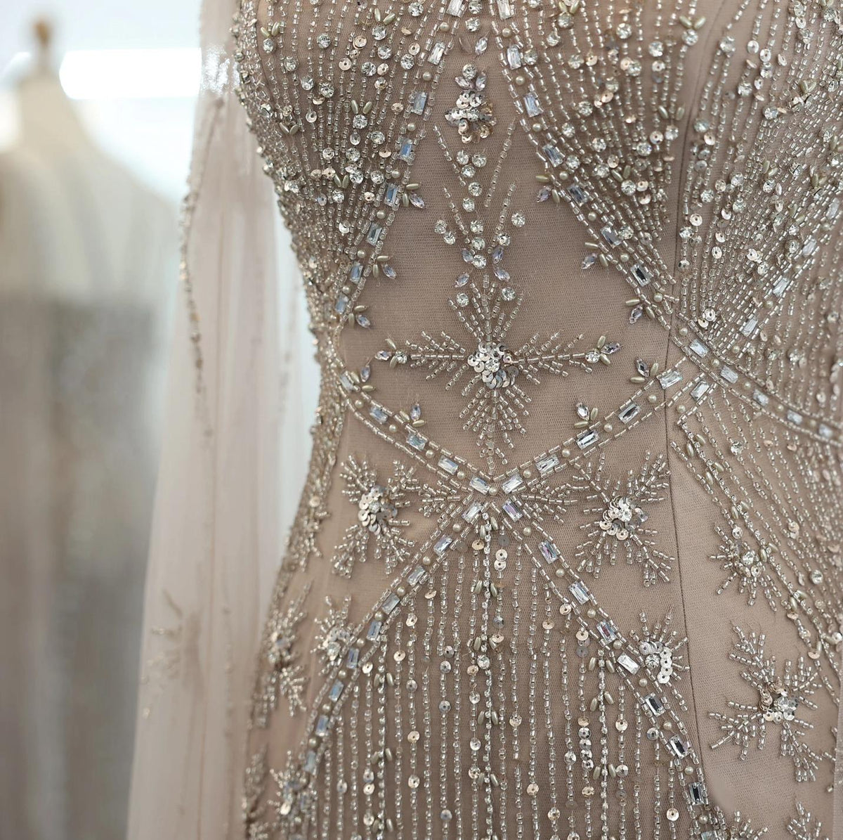 Close-up of a beige tulle gown featuring intricate silver beadwork, shimmering crystals, and sequin starburst patterns.