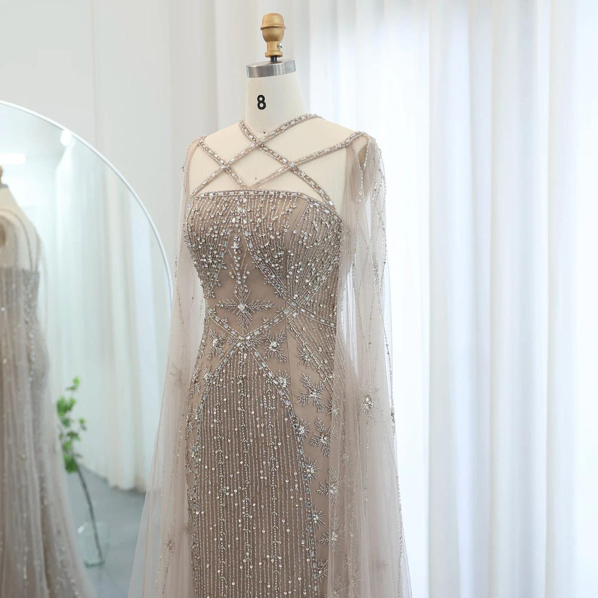 Beaded mermaid gown with tulle cape sleeves, criss-cross neckline, and intricate crystal and sequin embellishments.