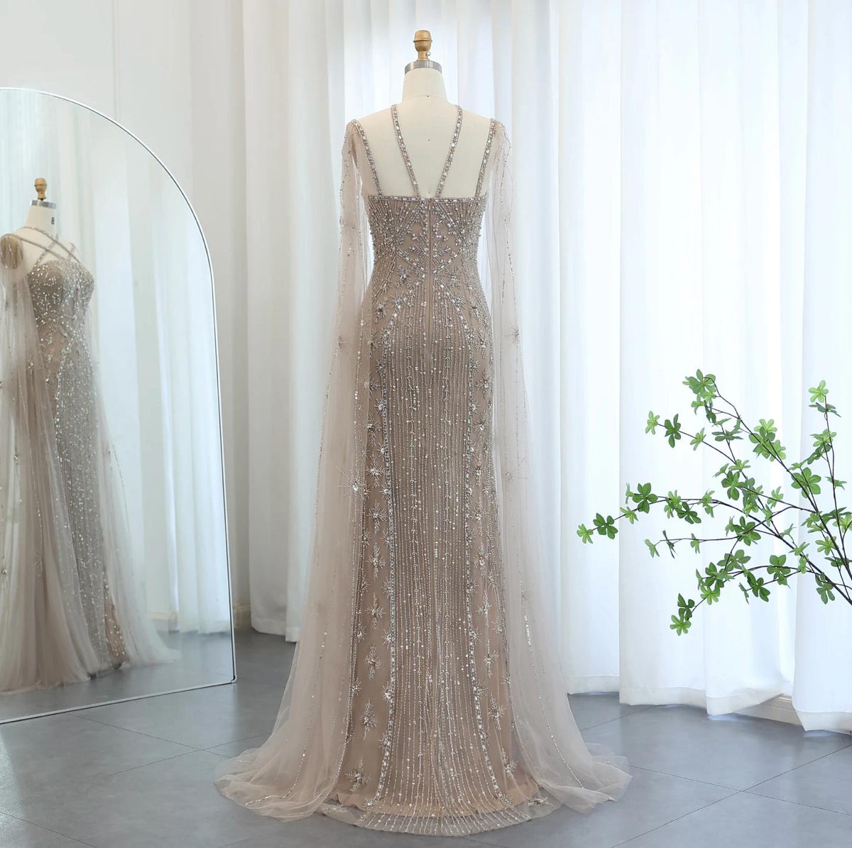 Beaded mermaid gown in champagne tulle with a criss-cross back, cape sleeves, and intricate crystal embellishments.