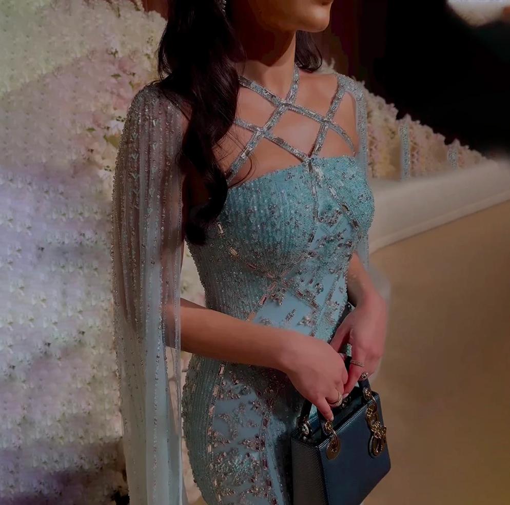 Light blue mermaid gown with beaded tulle, shimmering crystals, cape sleeves, and a criss-cross neckline.