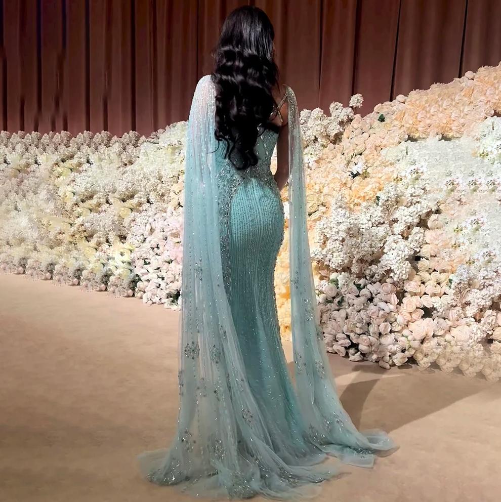 Back view of a light blue mermaid gown with beaded tulle, shimmering crystals, and dramatic flowing cape sleeves.
