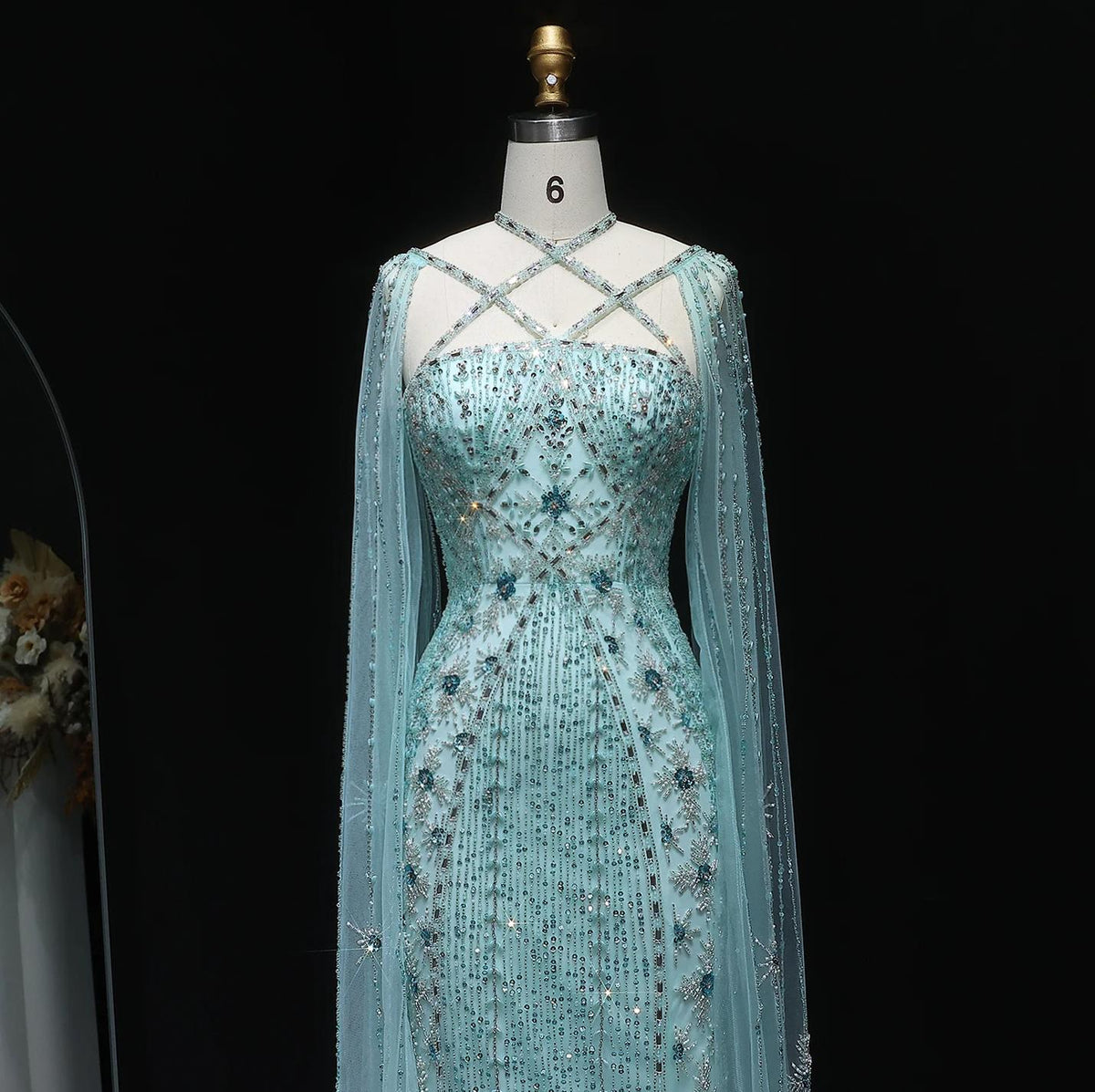 Light blue mermaid gown with a criss-cross neckline, cape sleeves, and intricate crystal and sequin beadwork on tulle.