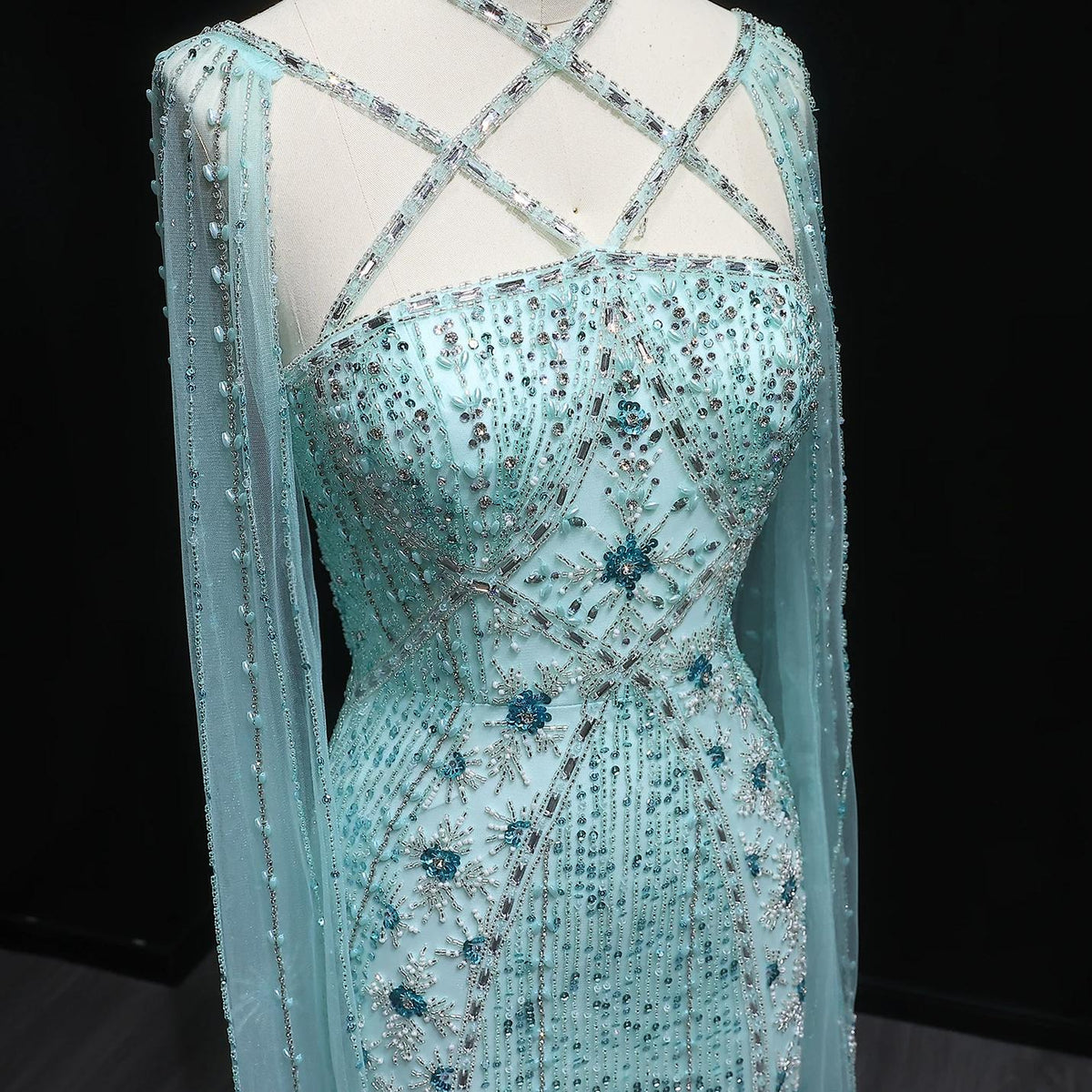 Light blue tulle mermaid gown with a criss-cross neckline, dramatic cape sleeves, and intricate crystal and sequin beading.