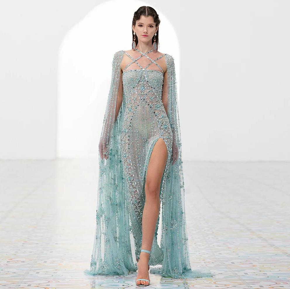 Beaded light blue mermaid gown with cape sleeves, criss-cross neckline, and high slit in shimmering tulle.
