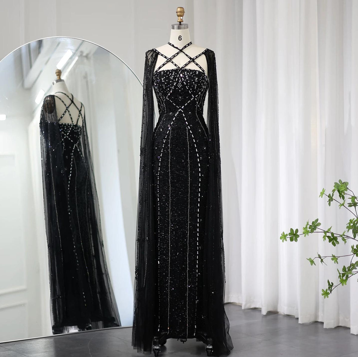 Black mermaid gown with cape sleeves, criss-cross neckline, and intricate crystal and sequin embellishments.