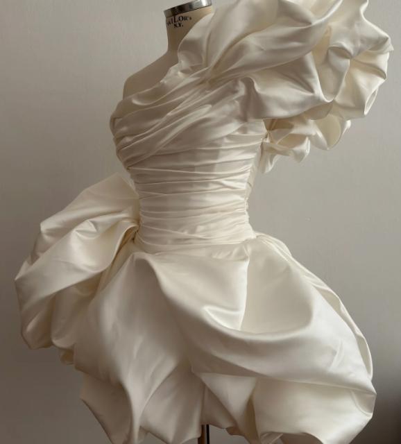 White mini taffeta prom dress with a ruched bodice, dramatic ruffled shoulder, and voluminous A-line skirt.