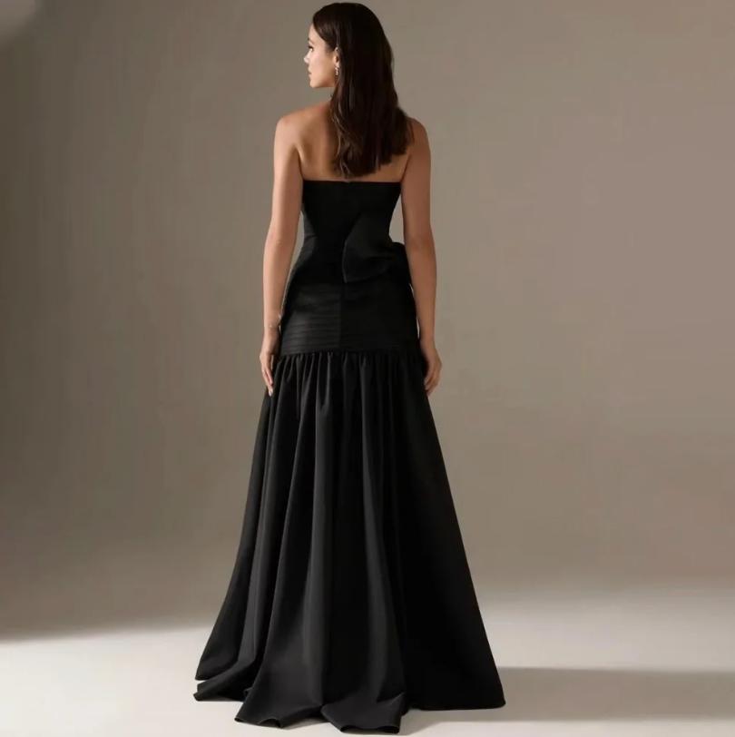 Back view of a black strapless satin A-line evening gown featuring a dramatic back bow and pleated floor-length skirt.